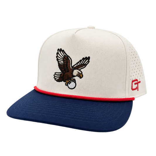 A structured trucker cap with an off-white crown, a navy blue flat brim, a red piping accent along the edge of the brim, and a brown and white embroidered bald eagle logo on the front. The side features a red 'CT' monogram on a perforated mesh panel.